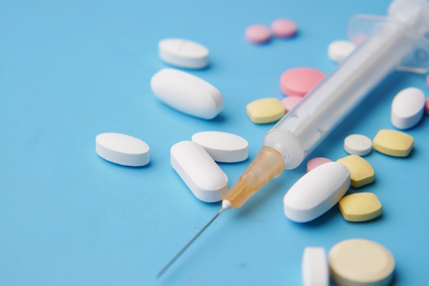 Syringe and pills on blue background close up