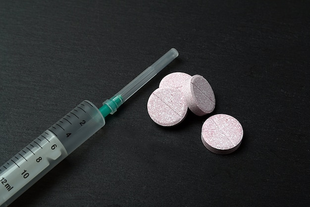 Syringe and pills isolated on black background