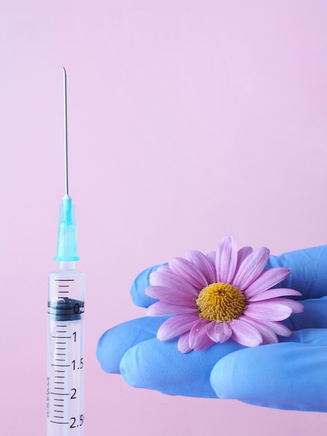 A syringe on a pink background and a hand with medical gloves of a nurse or doctor with a flower