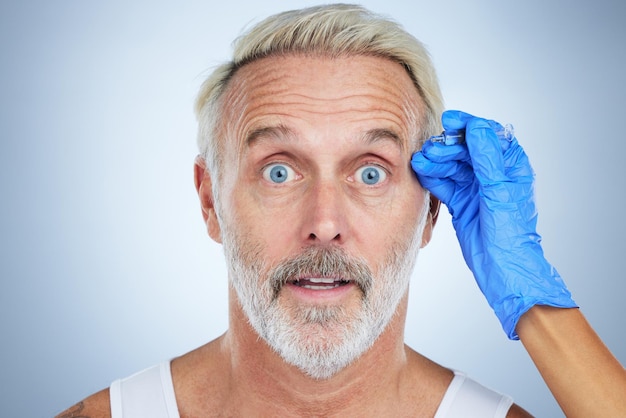 Портрет шприца и удивленный мужчина пожилого лица в студии, занимающейся пластической хирургией и косметическим уходом за кожей Дерматологические морщины и антивозрастное лечение зрелой модели с инъекцией наполнителя