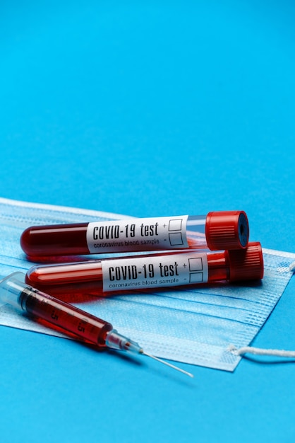 Syringe, test tube with blood sample and disposable face mask to prevent COVID-19 virus on blue