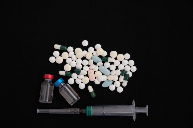 Photo a syringe two bottles of vaccine and a bunch of pills on a black background