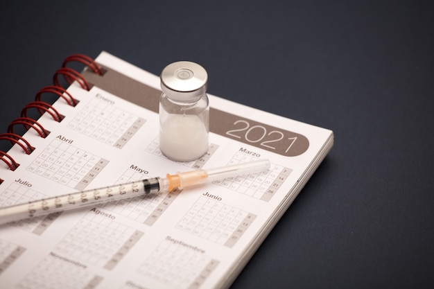 syringe and vaccine canister, with calendar 2021, blue surface