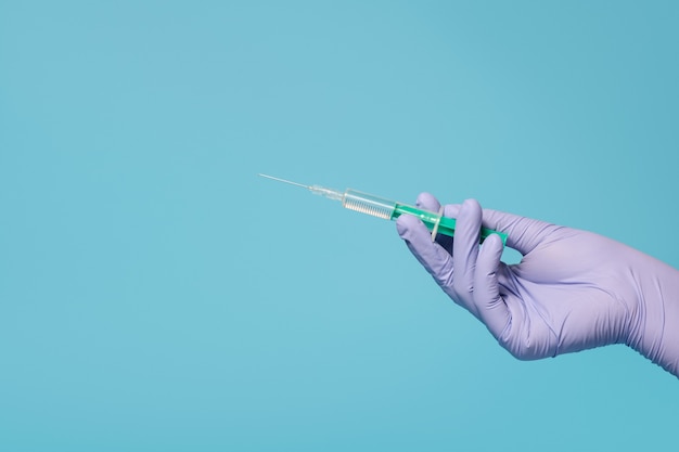 Syringe for vaccine injection in hand, latex medical gloves on hand. On a blue background.