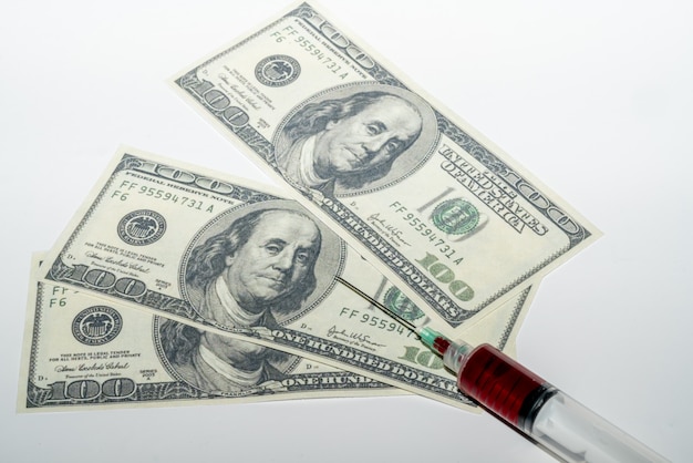 Syringe with blood on white background with money