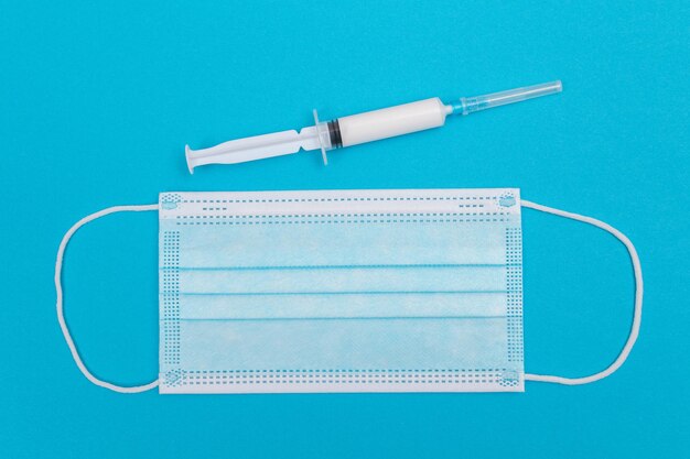 Syringe with medical mask on blue table  flat lay