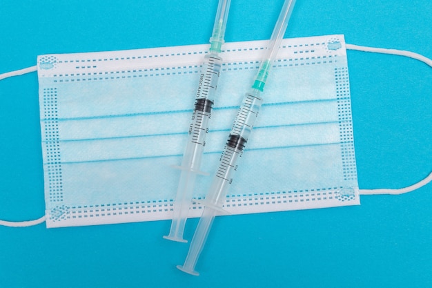 Syringe with medical mask on blue table  flat lay