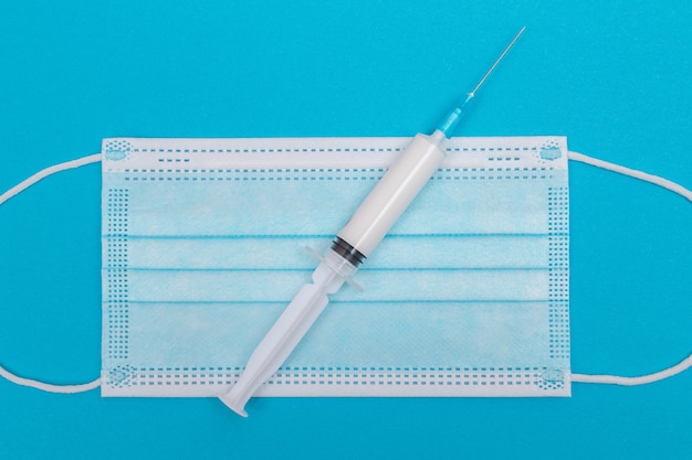 Syringe with medical mask on blue table  flat lay