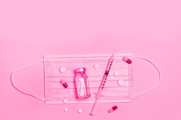 Syringe with medicine from a glass bottle, a protective medical mask on pink background. Vaccination against influenza, covid 19, measles, coronavirus disease. Vaccination and immunization concept