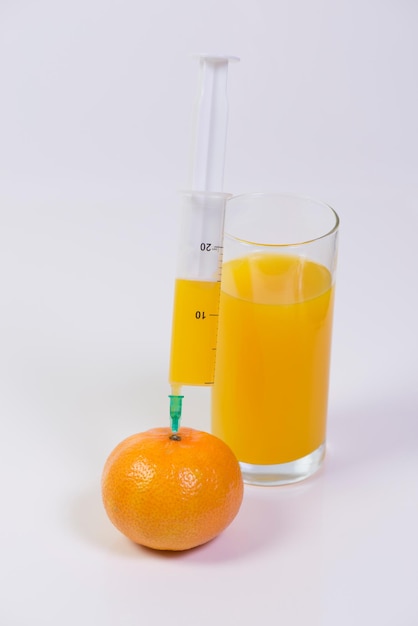 Syringe with orange fruit and juice on white background