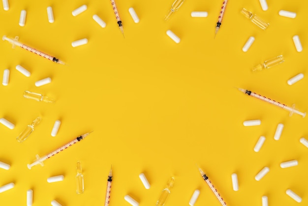 Syringes ampoules and pills on yellow background