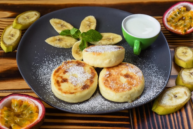 Syrniki or cheese pancakes with cream sauce and bananas on a plate on wooden table close up