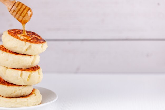 Syrniki - russian traditional cottage cheese pancakes with dripping honey dipper