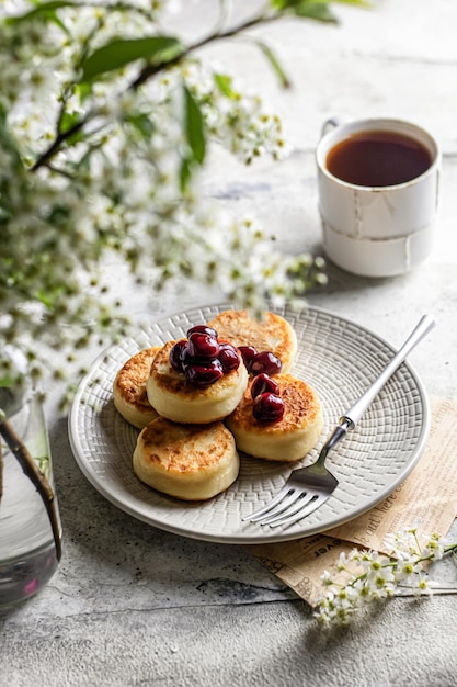 シルニキの伝統的なロシアのチーズパンケーキをチェリーと一緒に朝食に提供