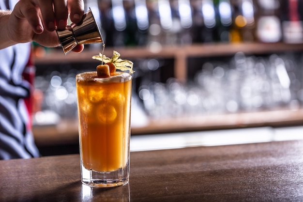 Syrup being pouredinto a golden cocktail in a bar by a had of the bartender.