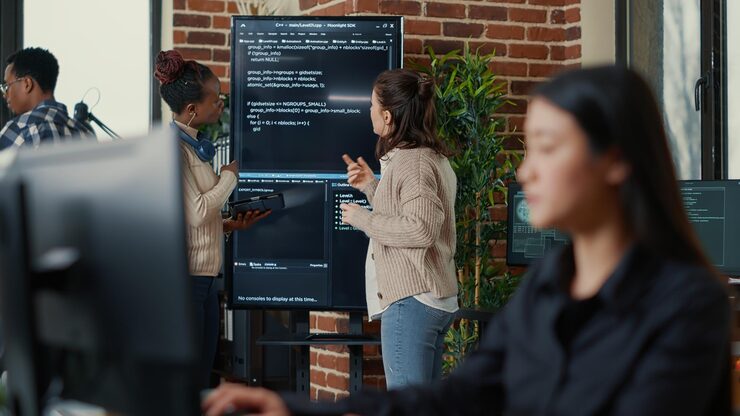 Photo system engineers comparing source code on wall screen tv analyzing errors using digital tablet with focus switching to programer writing algorithm. team of coders debugging machine learning data.