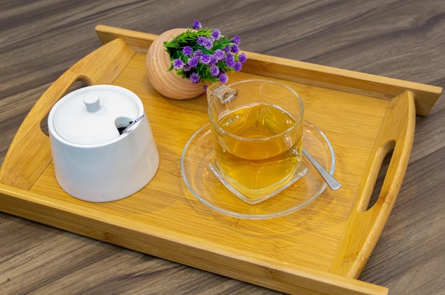 TÃÂÃÂ© caliente en taza de cristal. Colocado en una bandeja de madera decorada con un pequeÃÂÃÂ±o tarro de flores.