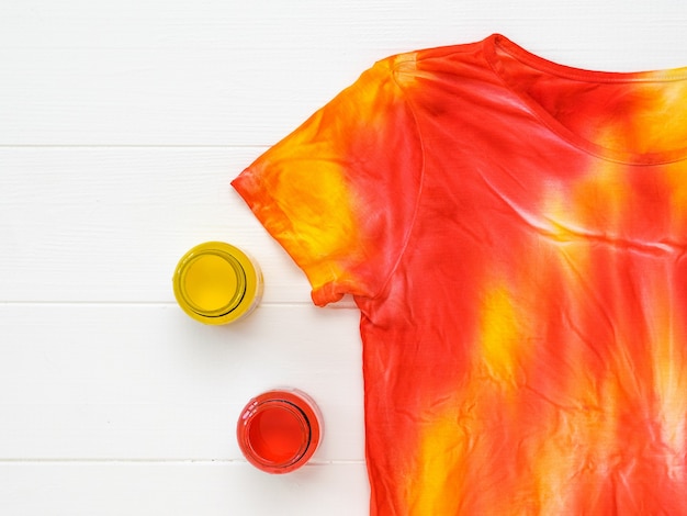 T-shirt decorated in the style of tie dye and jars of paint on a white table