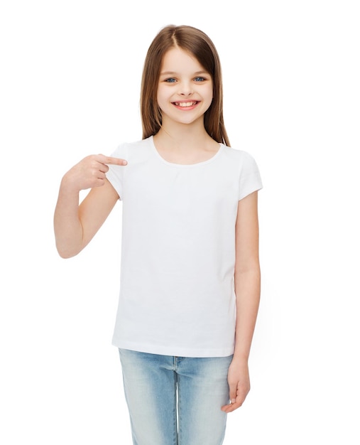 Concetto di design t-shirt - bambina sorridente in t-shirt bianca vuota che punta a se stessa