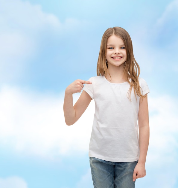 концепция дизайна футболки - улыбающаяся маленькая девочка в пустой белой футболке, указывающая на себя