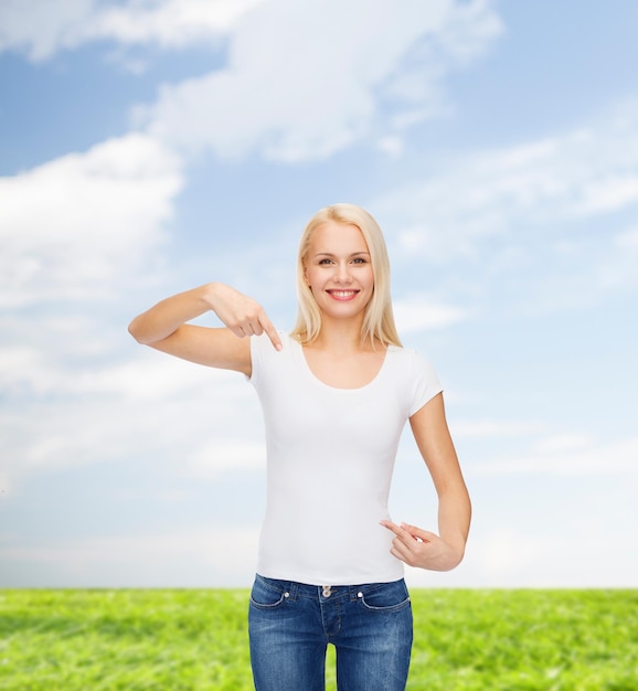 t-shirt design concept - smiling young woman pointing finger to blank white t-shirt