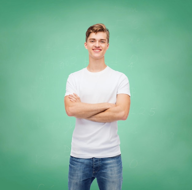 дизайн футболки, образование, школа, реклама и концепция людей - улыбающийся молодой человек в пустой белой футболке на фоне зеленой доски