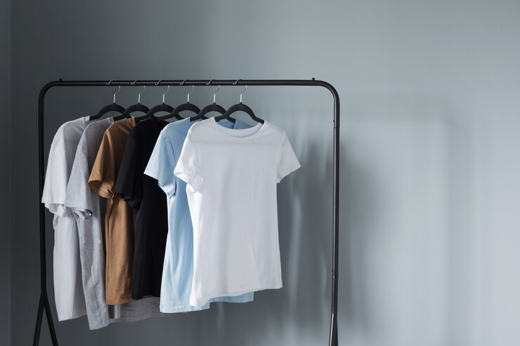 T-shirts of neutral colors on  black hanger against  gray wall