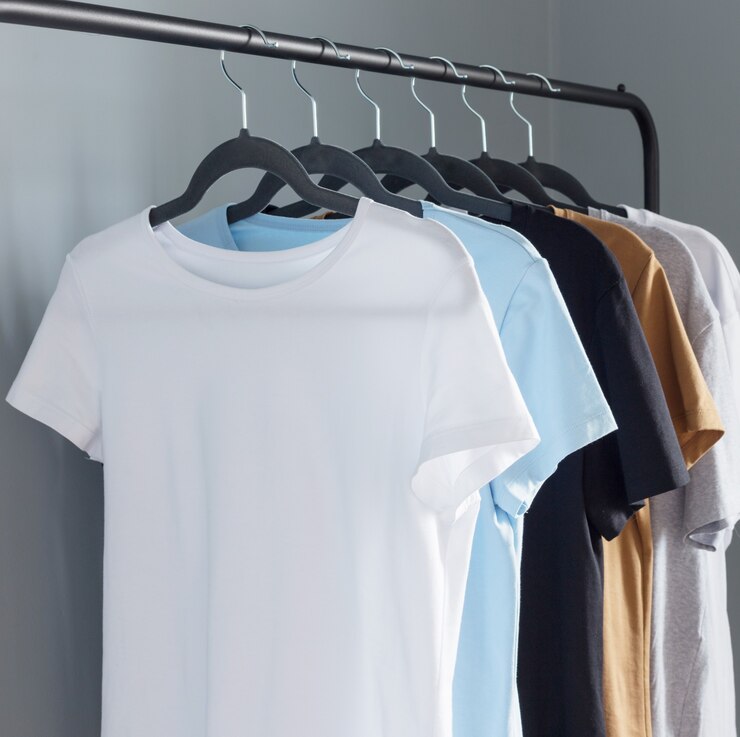 T-shirts van neutrale kleuren op zwarte hanger tegen grijze muur