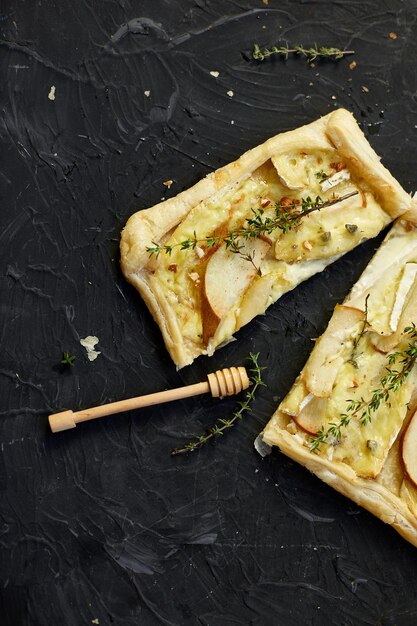 Taart gebakken in bladerdeeg met gorgonzola kaas en peren op zwarte tafel