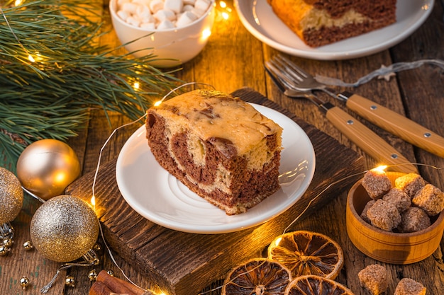 Taart op een feestelijke achtergrond met pijnboomtakken en een brandende slinger. Het concept van Kerstmis en Nieuwjaar. Zijaanzicht, horizontaal.