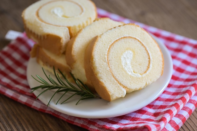 Taartbroodje op bord cake met rozemarijn op tafel biscuitbroodje plakjes snoep dessert roombroodje vanille snacks en voedselconcept Swiss Roll Cake