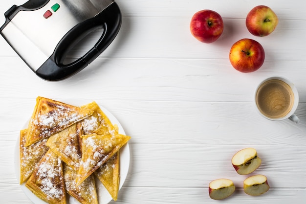 Taarten liggen op de tafel naast appels, een broodrooster en een kopje koffie