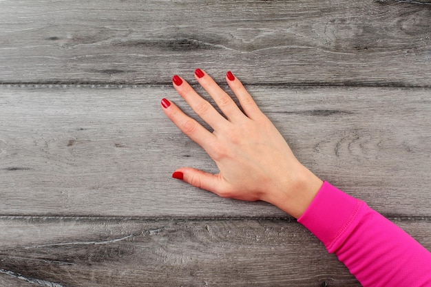 Tabel bovenaanzicht op jonge vrouw rechterhand met donkerrode nagels op lege grijze houten bureau.