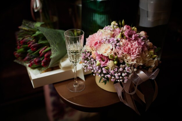 On the table are bouquets of flowers and glasses of champagne on the background of gifts.