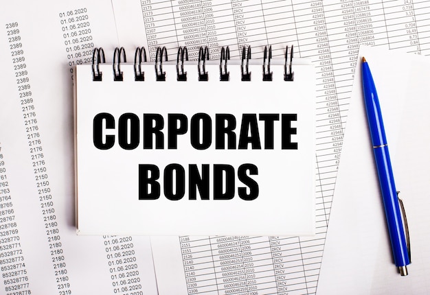 On the table are charts and reports, on which lie a blue pen and a notebook with the word CORPORATE BONDS