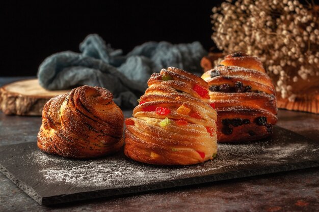 On the table are kraffins with raisins, candied fruits and poppy seeds, sprinkled with powdered sugar.