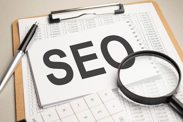 on the table are reports, a magnifying glass, a calculator, and a white notepad with the words seo. business concept