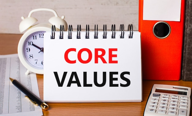 テーブルの上には、レポート、白い目覚まし時計、電卓、紙のフォルダー、ペン、そして「COREVALUES」というテキストが書かれた白いノートがあります。ビジネスコンセプト