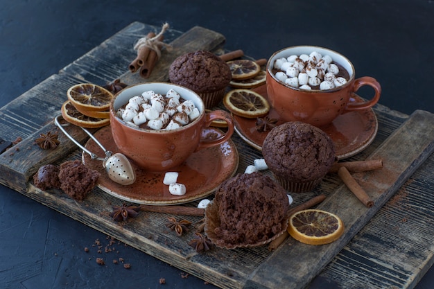 on the table are two cups of hot cocoa and marshmallows, chocolate muffins 