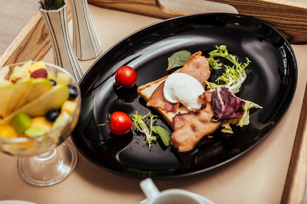 Table for bed. Breakfast from hotel kitchen consisting egg Benedict with tomatoes and fruit salad