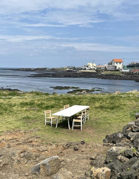 A table and chairs are set up on a grassy area overlooking the ocean.