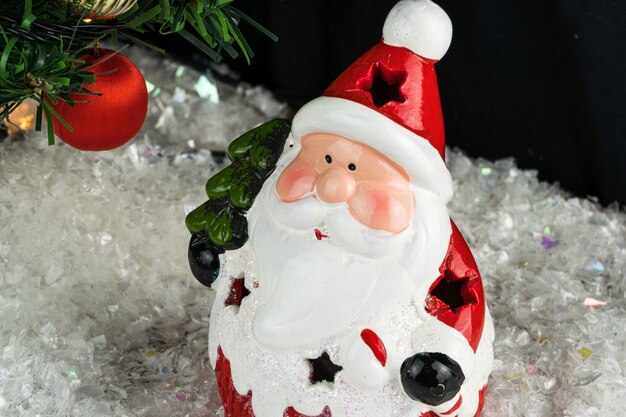 Table covered with snowflakes with Christmas decorations. Santa Claus, Christmas tree with red, gold balls and lights. Selective focus.