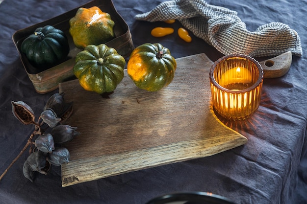 Украшение стола на Хэллоуин Зеленые тыквы на деревянной доске, свеча в оранжевой стеклянной свече