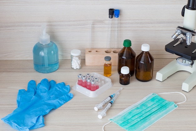 Sul tavolo: disinfettante per le mani, guanti, vaccini per fiale, siringhe, maschera per il viso, microscopio, compresse