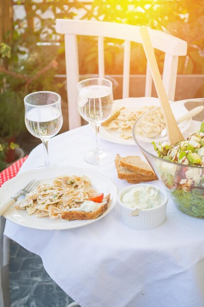 The table is covered with lunch with salad and pastas on the balcony sunny and warm atmosphere