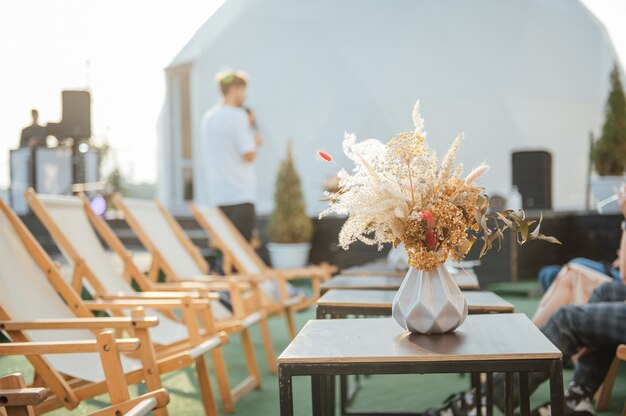 On the table is a decorative vase with dried flowers. Beautiful summer location for relaxation on a roof