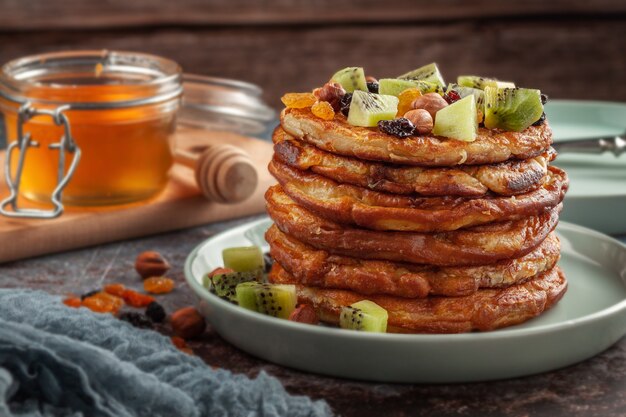 On the table is a dish with pancakes, honey, kiwi, nuts and raisins
