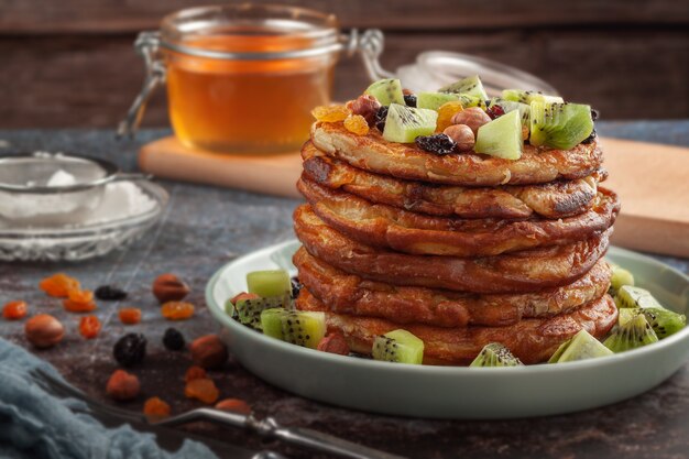 On the table is a dish with pancakes, honey, kiwi, nuts and raisins