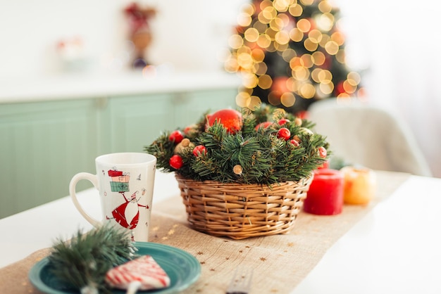 Foto la tavola è apparecchiata a festa per le candele rosse di natale e la disposizione dell'albero di natale nel cesto di vimini