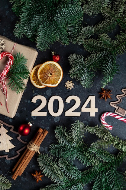 テーブルの上にはクリスマス ツリーの枝の木のおもちゃのスパイスと数字 2024 に囲まれたギフトです。